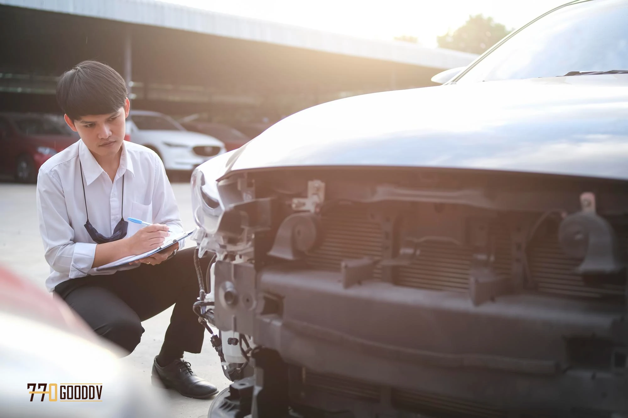 An insurance assessor meticulously examining the damage to a car's front end, taking notes on a clipboard during a bright, hazy day, with a focus on informed vehicle valuation after an accident.